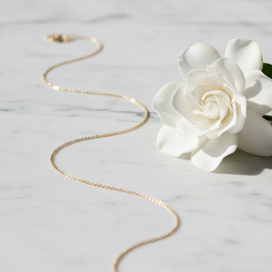 14kt gold delicate chain necklace draped on white marble with gardenia flower